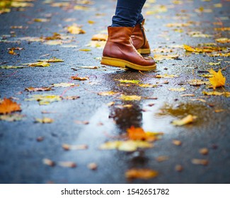 Walk On Wet Sidewalk. Back View On The Feet Of A Woman Walking Along The Asphalt Pavement With Puddles In The Rain. Pair Of Shoe On Slippery Road In The Fall. Abstract Empty Blank Of The Autumn Weathe