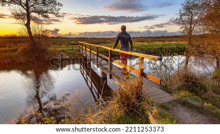 Walker crossing bridge over river in dutch countryside National Park landscape the Drentsche Aa, Drenthe Province, the Netherlands