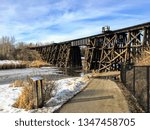 Walking along a pathway beside the Sturgeon River in St. Albert, Alberta, Canada.  The snow and ice are melting and there is an old wooden train bridge in the background.