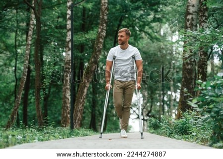 Walking in the beautiful park. Man with crutches is outdoors. Having leg injury.