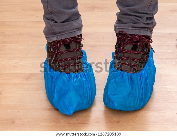 Walking\
boots and feet in blue plastic shoe protectors, covers. Hygiene in\
medical situations etc. Single use,\
disposable.