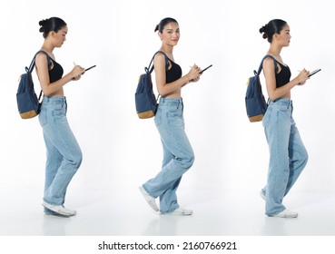 Walking With Cell Smart Phone Full Length Figure Snap Of 20s Asian Woman Black Hair Vast Jeans Pant And Sneaker. Casual Beautiful Female Walk With Backpack Over White Background Isolated