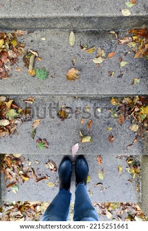 Walking up cement stairs in rain boots in autumn with fall leaves on the ground