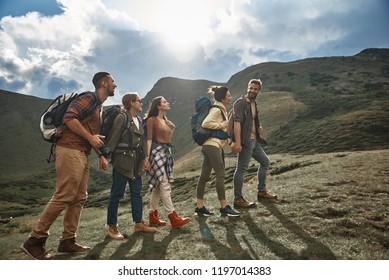 Caminando. Alegres amigos activos vistiendo ropa cómoda y llevando mochilas mientras disfrutan de su viaje por la montaña