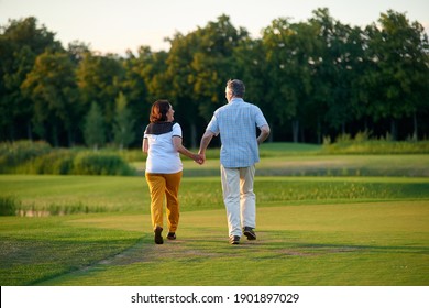 Walking couple on the field. Mature man and his wife on the green lawn.