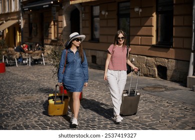 walking down, city sidewalk, sunny street. Two casually dressed young women walk down cobblestone street with suitcases, enjoying sunny day in urban setting. - Powered by Shutterstock