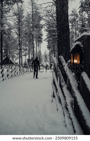 Walking down snowy path past wooden fences and lanterns in Santa Claus' Village on winter day in Rovaniemi, Lapland, Finland