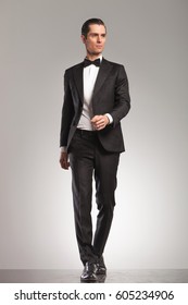 Walking Elegant Man In Tuxedo Is Looking Up To Side On Grey Studio Background