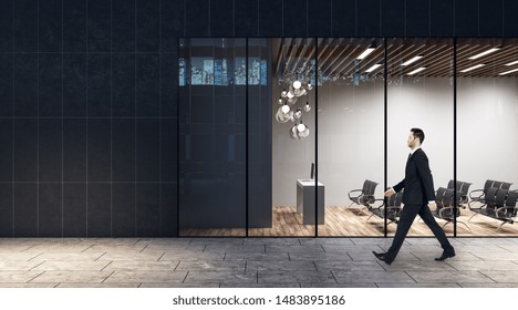 Walking in the evening on a street businessman past business center with minimalistic style auditorium with lights, black chairs and wooden floor. - Shutterstock ID 1483895186