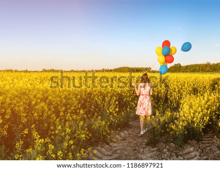 walking girl with bunch of balloons in blooming field