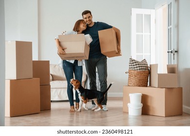 Walking, holding boxes and smiling. Young couple with dog are moving to new home. - Powered by Shutterstock