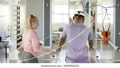Walking man in purple tee using parallel bars in rehab gym, therapist guiding with orange harness. Gait, training, mobility, balance, clinician, trainer, mirrors
