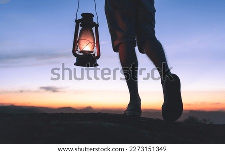 Walking at night while carrying a kerosene lamp to light the way, with sky after sunset in the background. Taking steps on the path of faith and spirituality.