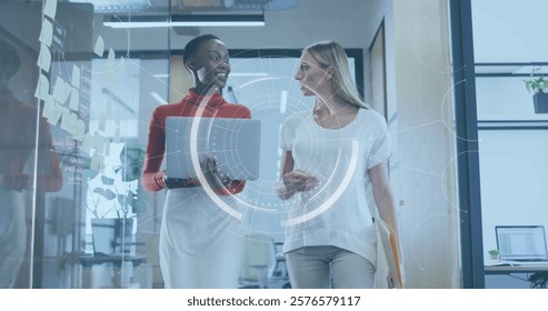 Walking in office, two businesswomen with digital interface image over them. technology, teamwork, innovation, collaboration, diversity, professional