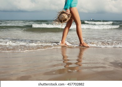 Walking On The Beach. Close Up On Legs Walking Along The Sea Side, Woman With Straw Hat Enjoy Freedom On Beautiful Ocean 