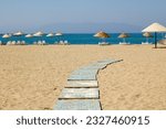 Walking path on the hot sand at the beach with blurred wicker umbrellas and sun loungers