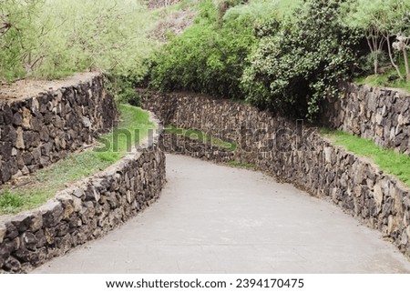 Walking path on Tenerife island. Rock solid wall among pavement. Brick wall road. Stones border. Walking down the hill. Empty pavement in nature.