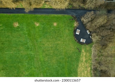 Walking path in a park with green fields and trees and small picnic area with tables and benches. Aerial top down view. Nature scene. Nobody.
