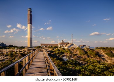 A walking ramp that leads the view to a majestic lighthouse in Oak Island Beach in North Carolina. This image was taken during a sunny afternoon in spring season.