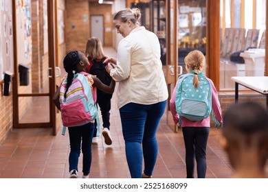 Walking in school hallway, female teacher guiding diverse students with backpacks to classroom. Education, mentoring, teaching, guidance, learning - Powered by Shutterstock