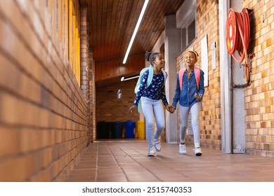 Walking in school hallway, two african american girls with backpacks smiling and holding hands. Friendship, students, education, bonding - Powered by Shutterstock