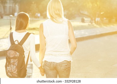 Walking Side By Side. Horizontal Shot From Behind Of Mother Walking Her Teen Daughter With A Backpack To School Holding Hands