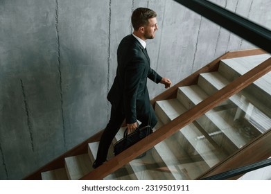 Subiendo. Hombre con traje de negocios y corbata con el caso en las manos está en las escaleras.