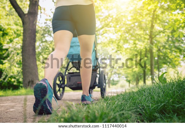 Walking woman with baby stroller enjoying summer\
day in park. Jogging or power walking supermom, active family with\
baby jogger.