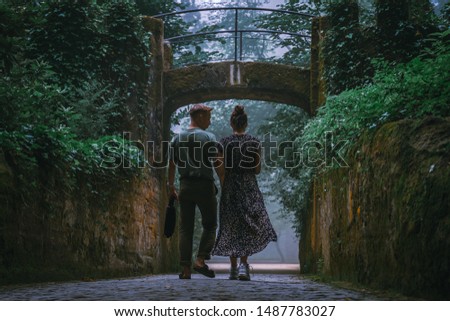 walking young couple in mysterious foggy forest. fantasy woods scenery with fog between trees on background. man and woman enjoying view. Portugal, Sintra, Quinta da Regaleira 