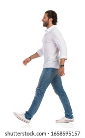 Walking Young Man In Jeans, Sneakers And White Shirt. Side View. Full Length Studio Shot Isolated On White.