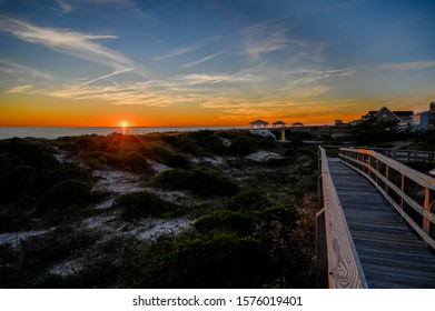 A walkway along the sand dunes with the sun setting over the ocean.