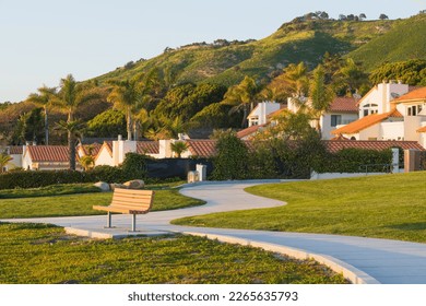 Walkway along the shore and wooden bench overlooking the ocean, and beautiful houses and green hills in the background, California - Powered by Shutterstock