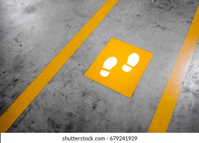 Walkway lane in parking building. Painted yellow footsteps between parallel yellow lines on abstract cement floor. Step by step concept.