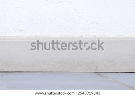 Wall baseboard between blurred floor and white wall texture background. Front view of wall and wooden baseboard for interior, old house, aged, and material. Texture background of baseboard and cement.