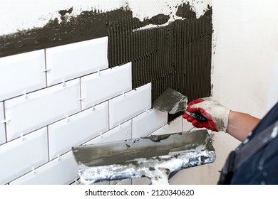 Wall Cladding. The Master's Hands Apply Tile Glue To The Walls Using Two Spatulas Or Trowels Of Different Sizes. Selective Focus