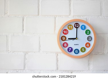 Wall clock with colored dial time 9 am or 9 pm on a white brick wall. Workday morning, time concept. Place for text. Close-up.