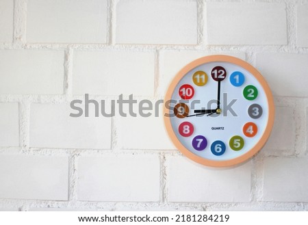 Wall clock with colored dial time 9 am or 9 pm on a white brick wall. Workday morning, time concept. Place for text. Close-up.