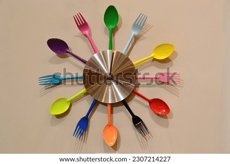 Wall clock with colorful forks and spoons hanging on isolated white wall.