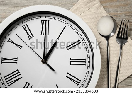 Wall clock and cutlery on light wooden table, closeup. Business lunch concept