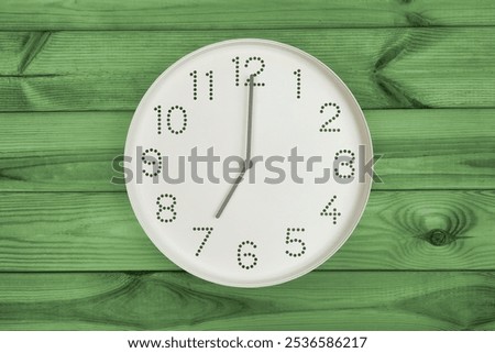 Wall clock shows time 7 o'clock on green wooden background. Round wallclock front view. Nineteen o'clock. brand new day, fresh start, fresh energy, new opportunities