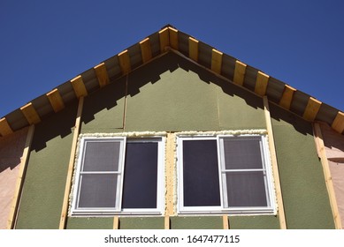 Wall Covering Of The Frame House With Panels Of Vinyl Siding. Construction Or Reconstruction, Repair Of The House. Installation Of Plastic Windows In A New Residential Building On Blue Sky Background.