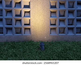 A wall with a cylindrical light source and a grassy area in front