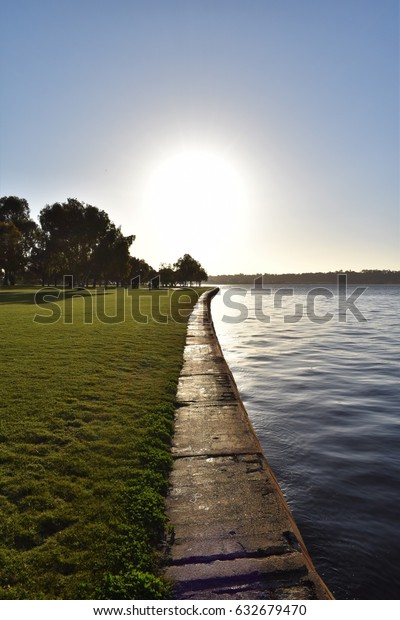 Wall dividing the river and the lawn with sun\
in the background