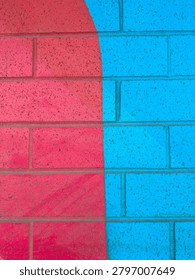 A wall features two sections, one red and one blue, creating a bright visual contrast. The sunlight enhances the colors of the paint and reveals the texture of the bricks.