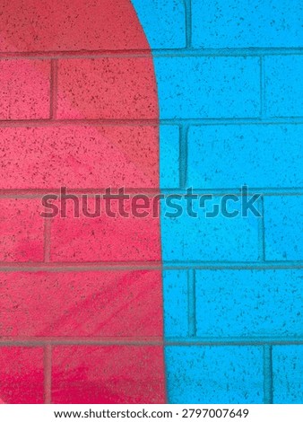 A wall features two sections, one red and one blue, creating a bright visual contrast. The sunlight enhances the colors of the paint and reveals the texture of the bricks.