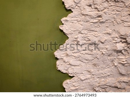 A wall featuring peeling plaster that partially exposes green paint, creating a distressed textured background.