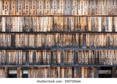Wall full of weathered wood boards (ema) with the names of the donors and dates at the entrance of the Fushimi Inari Shrine in Kyoto, Japan.