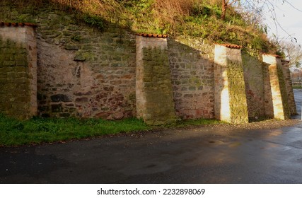 The wall of the garden reinforced on the back with brick pillars. Supports such a long wall and increases stability in wind and frost movements of the unstable subsoil. tile, roof, clay, slope hill - Shutterstock ID 2232898069