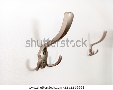 Wall hanger hook isolated on white background. Close up of matt chrome coat rack on white wall. Wall coat rack screwed to the wall.