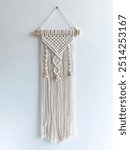 Wall Hanging Macrame made of white cotton rope filled with wooden beads hanged on the white wall 